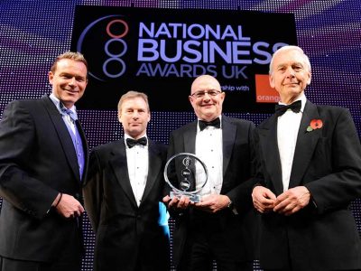 Four people in suits holding an award at the National Business Awards UK event.