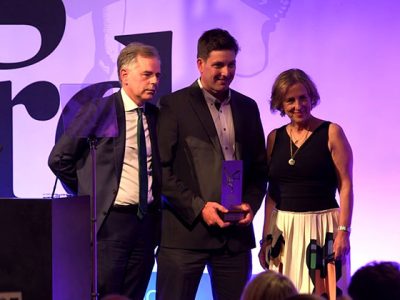 Three people on stage with an award, at a formal event.