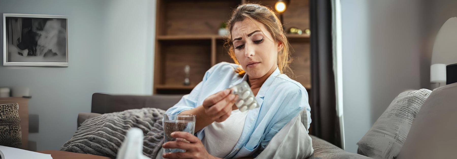 Person in a robe holding a pill blister and a glass of water on a couch, discussing their ace Medicare supplement plan.