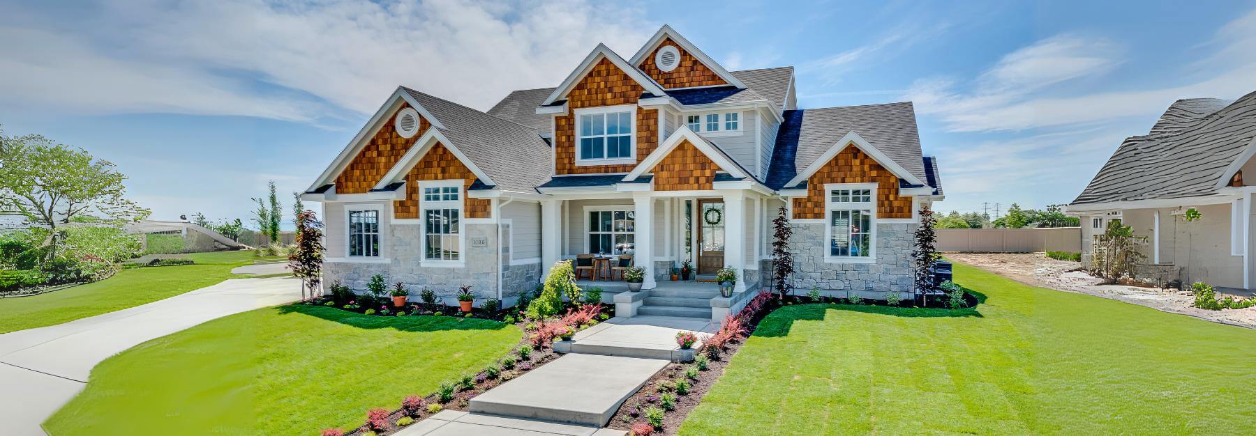 New two-story suburban house with a stone and wooden façade, a beautifully landscaped lawn, a shed with porch, and a clear blue sky.